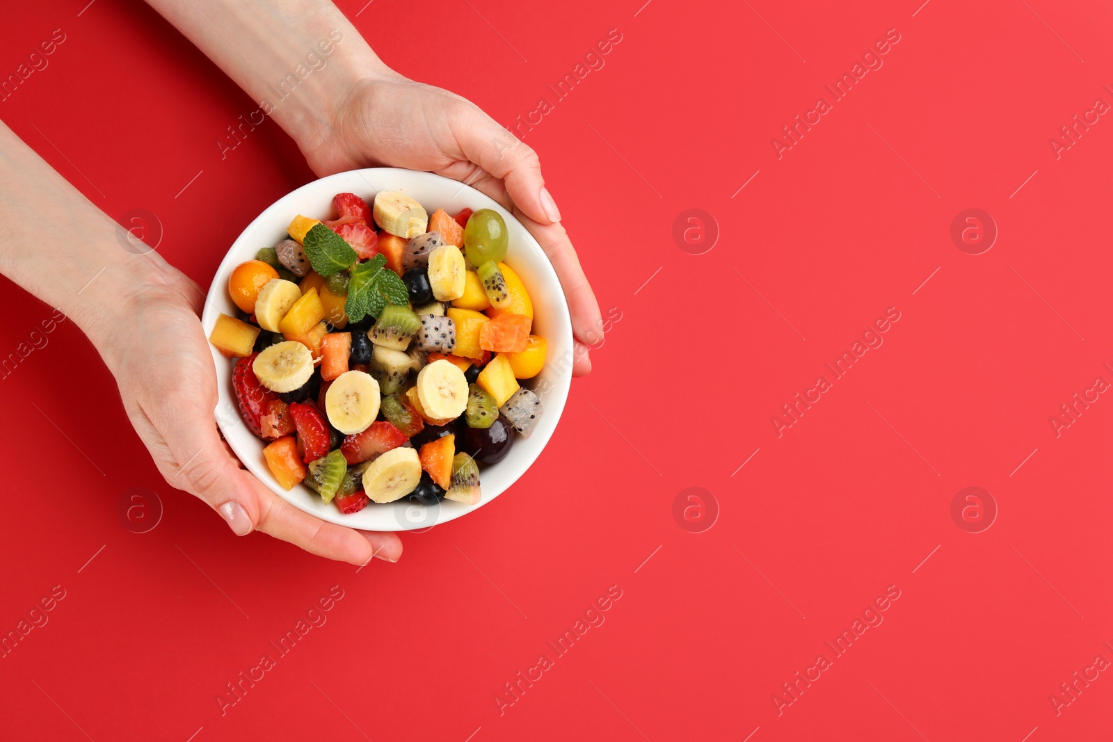Photo of Woman with delicious exotic fruit salad on red background, top view. Space for text