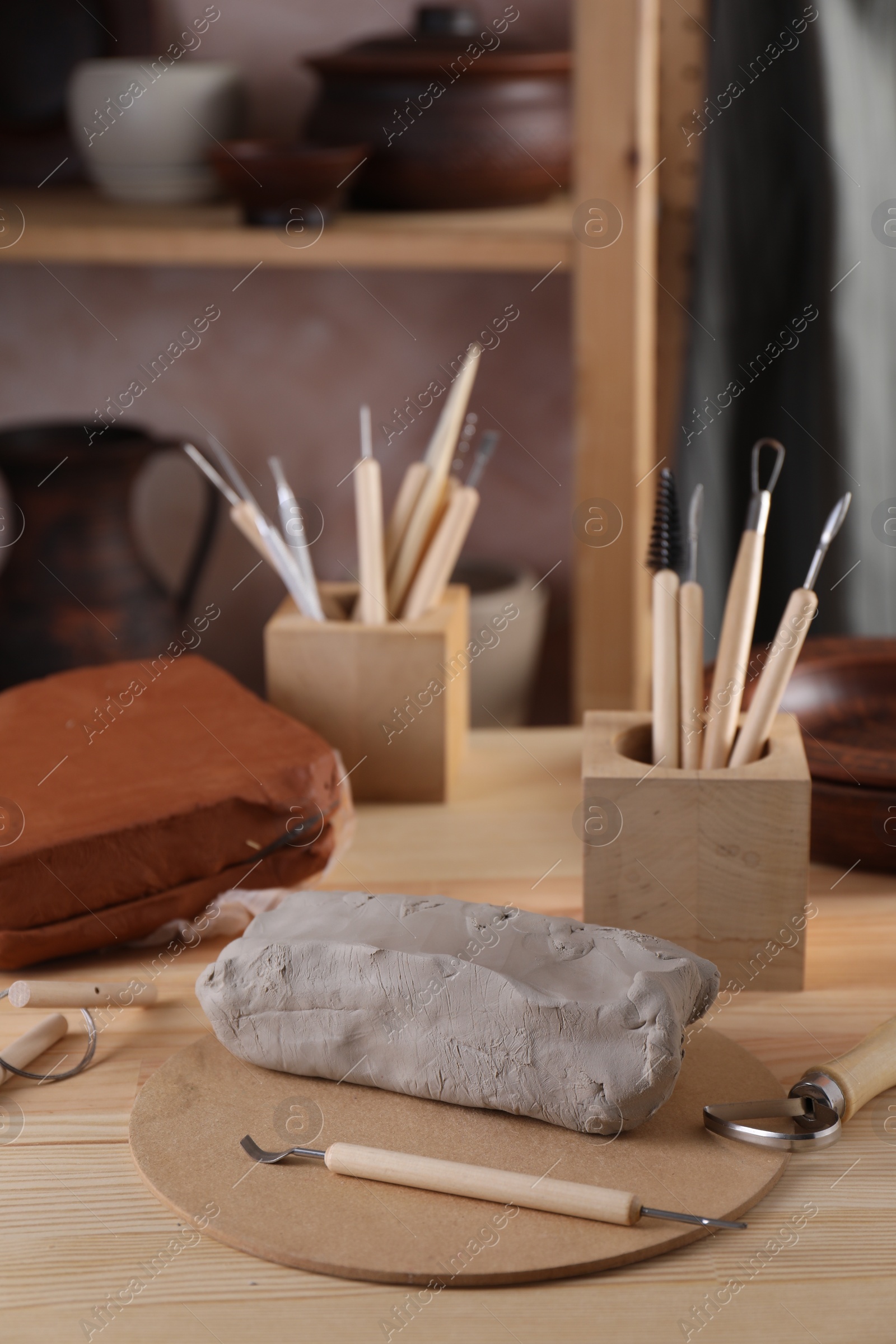 Photo of Clay and set of modeling tools on wooden table in workshop