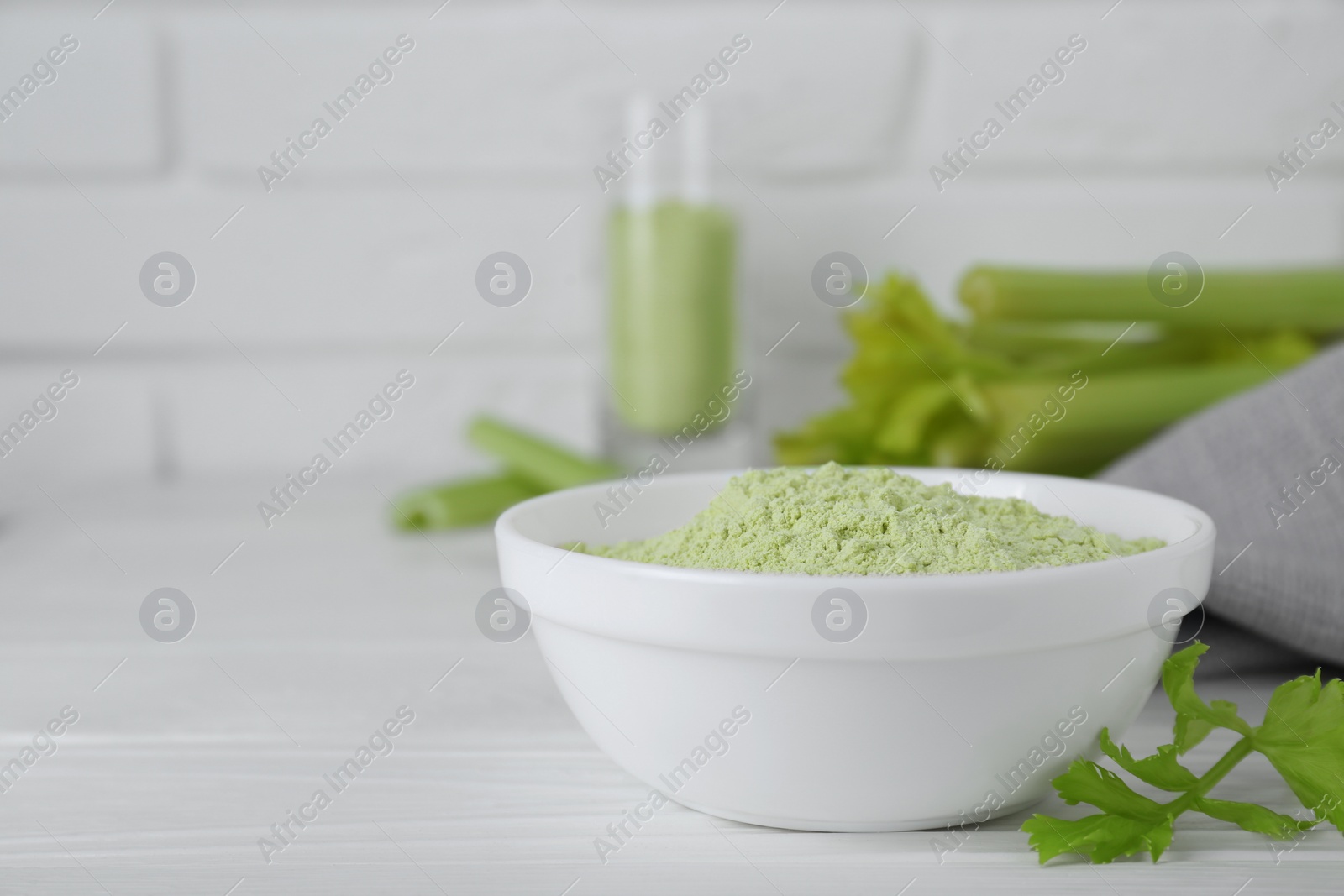 Photo of Natural celery powder in bowl and fresh stalks on white table, closeup. Space for text