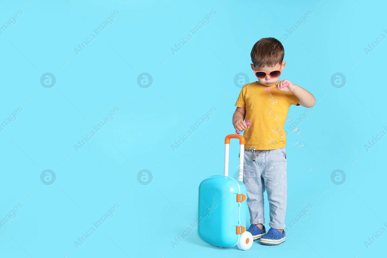 Photo of Cute little boy with sunglasses and suitcase on blue background, space for text