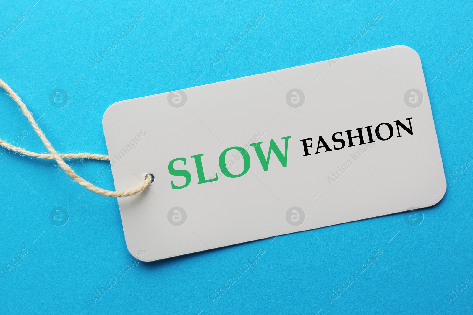 Image of Conscious consumption. Tag with words Slow Fashion on light blue background, top view