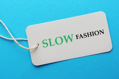 Image of Conscious consumption. Tag with words Slow Fashion on light blue background, top view