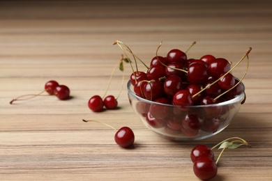 Photo of Glass bowl of delicious cherries on wooden table, space for text