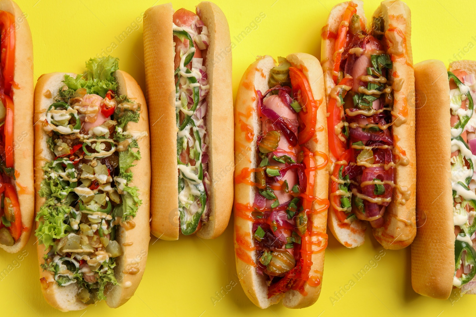 Photo of Delicious hot dogs with different toppings on yellow background, flat lay