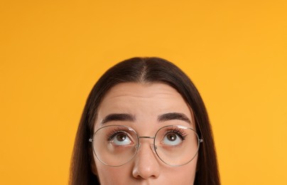 Woman in glasses looking up on orange background, closeup
