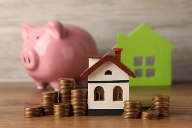 Photo of House models, piggy bank and stacked coins on wooden table, selective focus