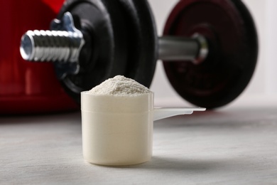 Photo of Measuring scoop of protein powder and dumbbell on white table, closeup