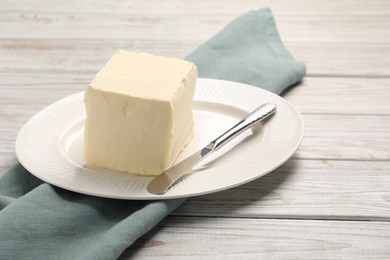 Block of tasty butter and knife on white wooden table