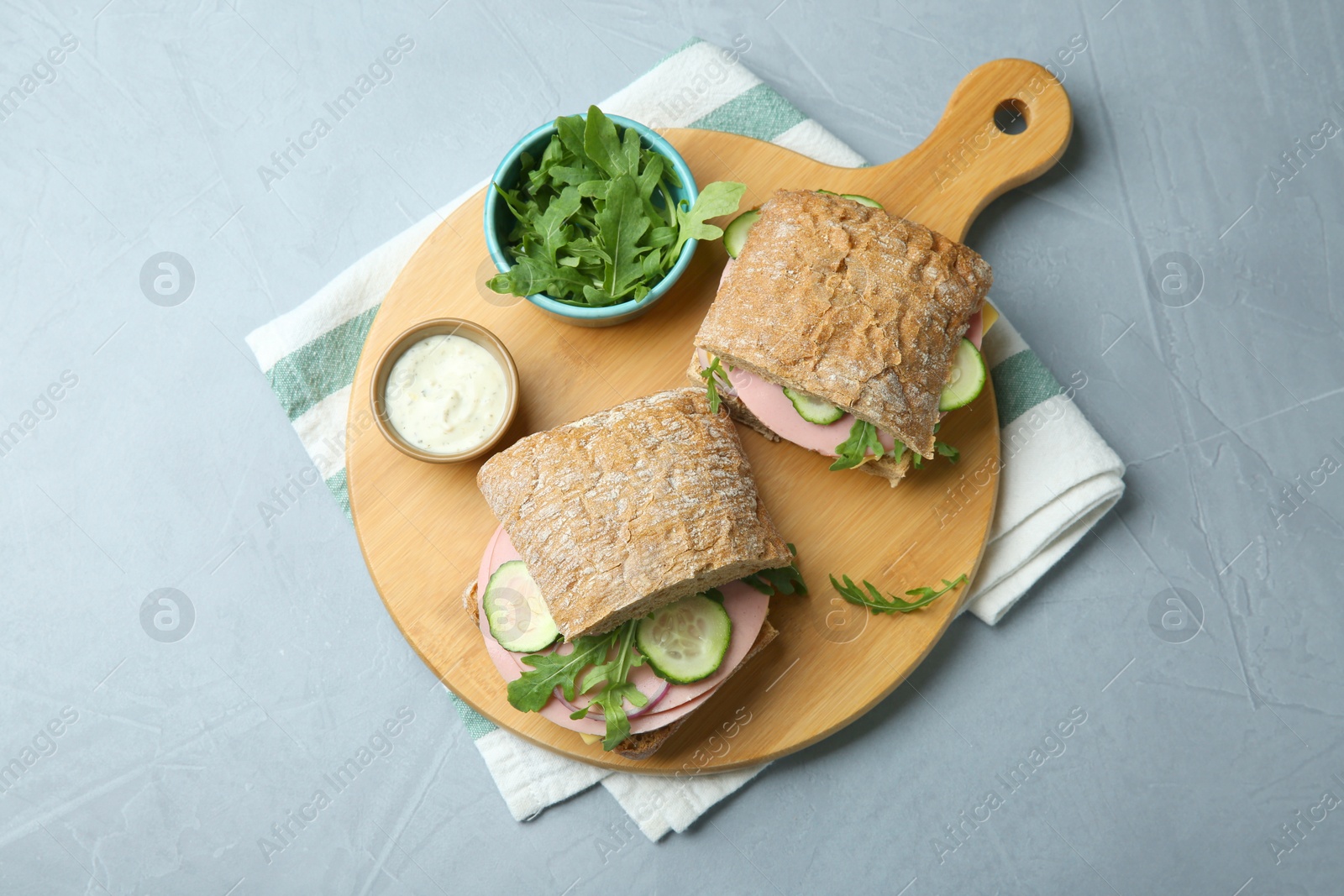 Photo of Tasty sandwiches with boiled sausage, cucumber, arugula and sauce on grey table, top view