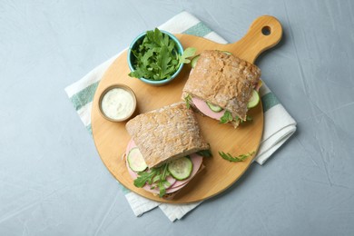 Tasty sandwiches with boiled sausage, cucumber, arugula and sauce on grey table, top view