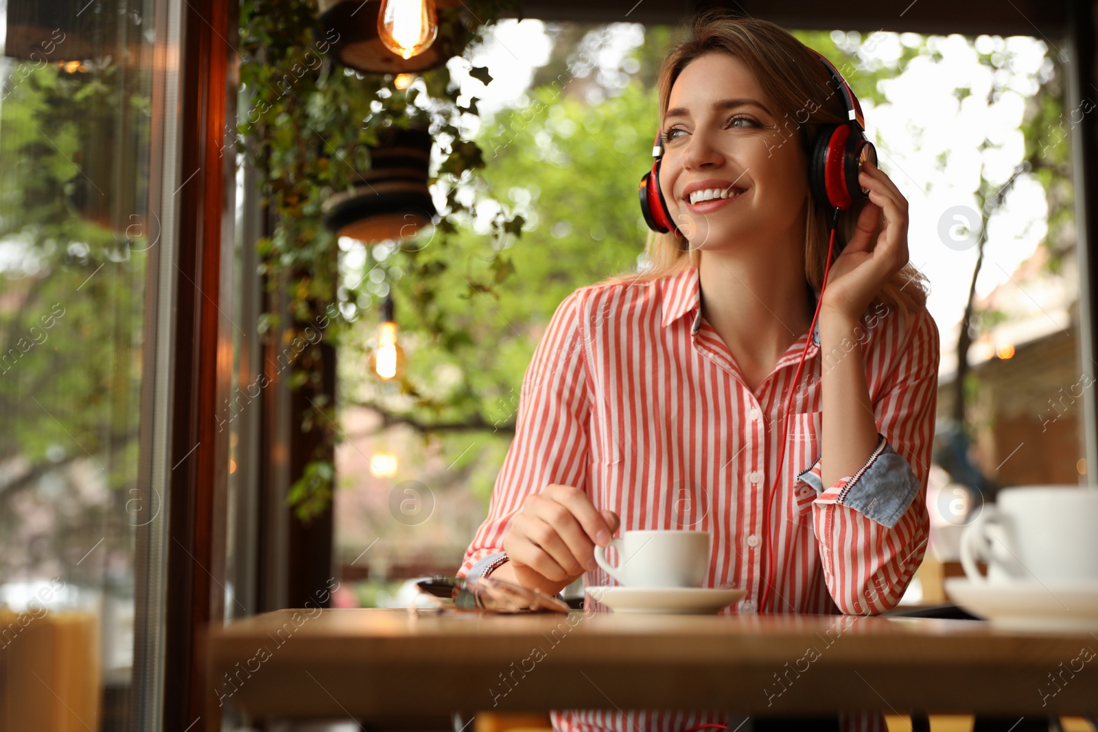 Photo of Young woman with headphones listening to music in cafe