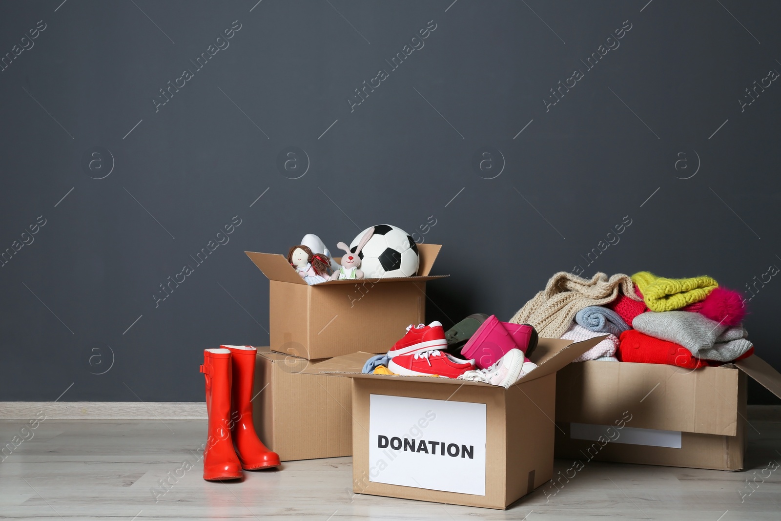 Photo of Carton boxes with donations on floor near grey wall. Space for text