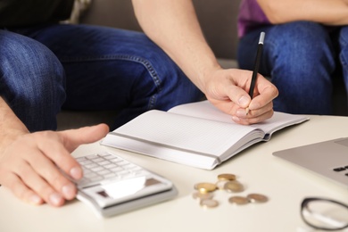 Man counting money with calculator at table, closeup