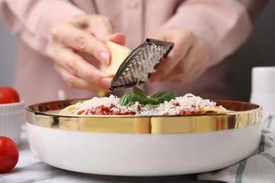 Photo of Woman grating parmesan cheese onto delicious pasta at white marble table, closeup