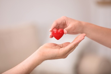 Woman giving red heart to man on blurred background, closeup. Donation concept