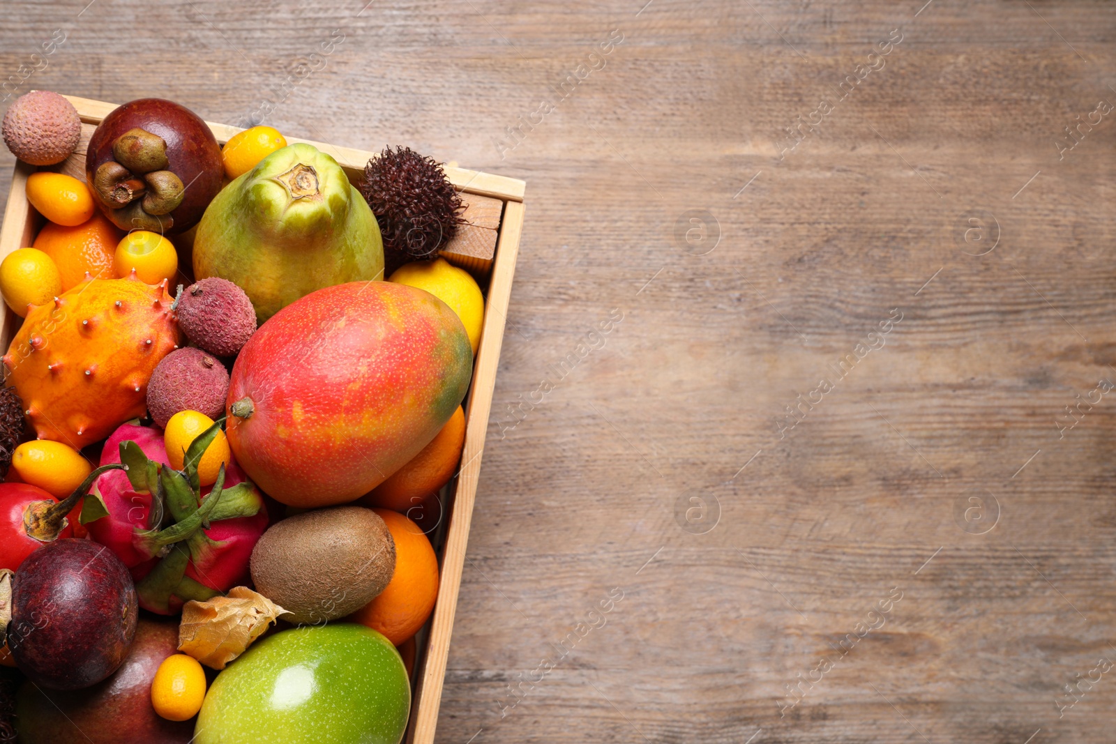 Photo of Crate with different exotic fruits on wooden table, top view. Space for text