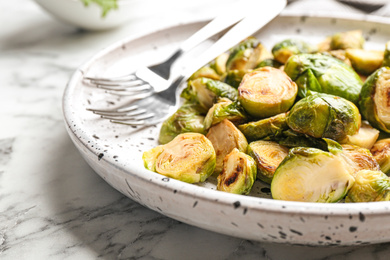 Photo of Delicious roasted Brussels sprouts on white marble table, closeup