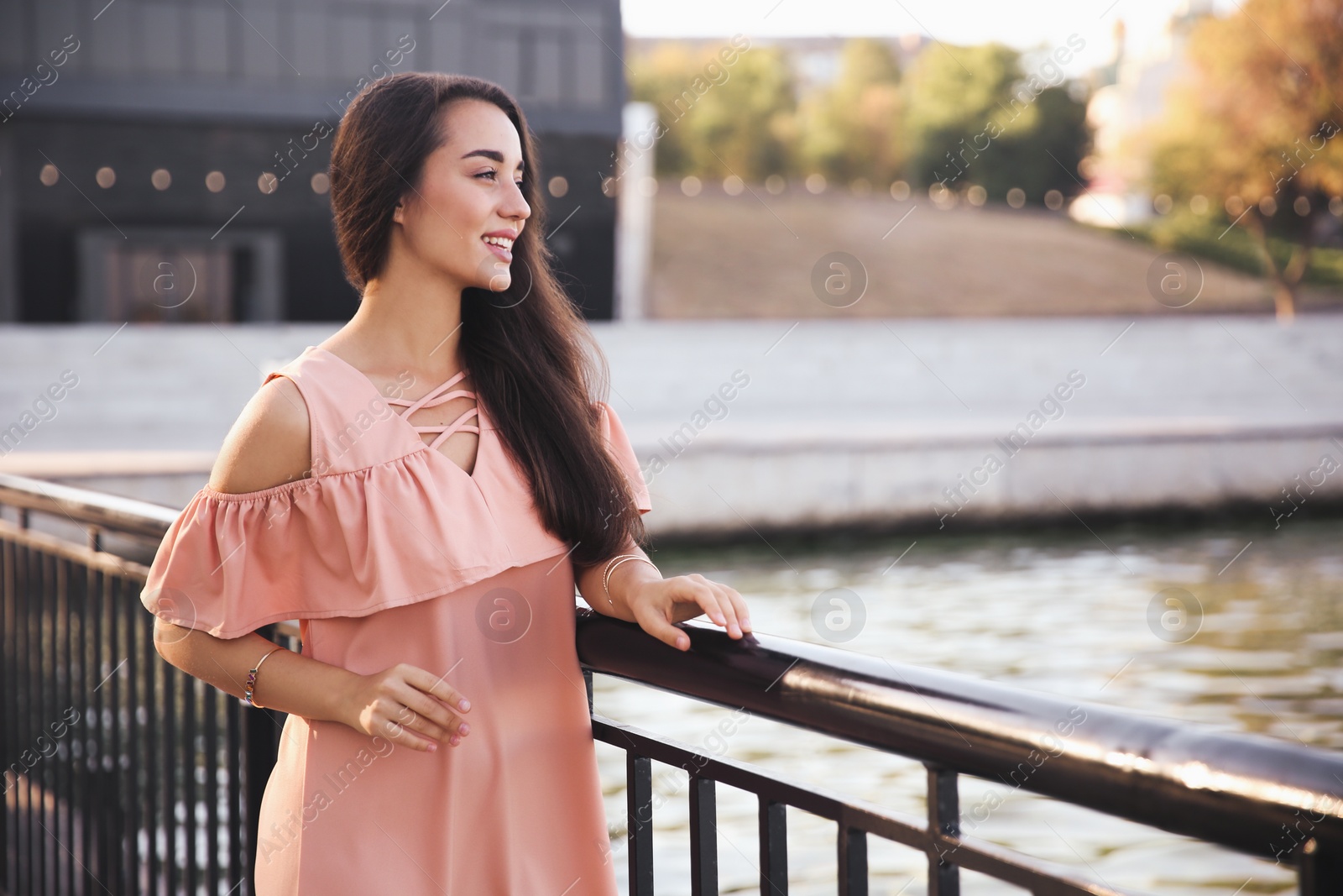 Photo of Beautiful young woman in stylish pink dress near railing on pier