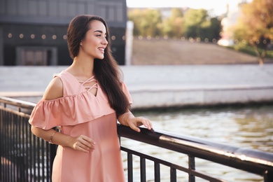 Photo of Beautiful young woman in stylish pink dress near railing on pier