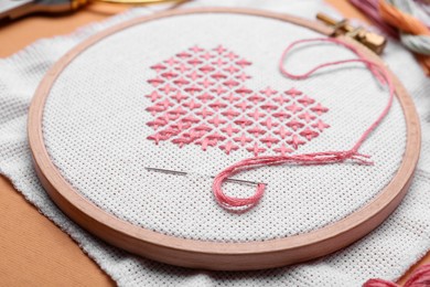 Canvas with embroidered heart and needle in hoop on orange background, closeup