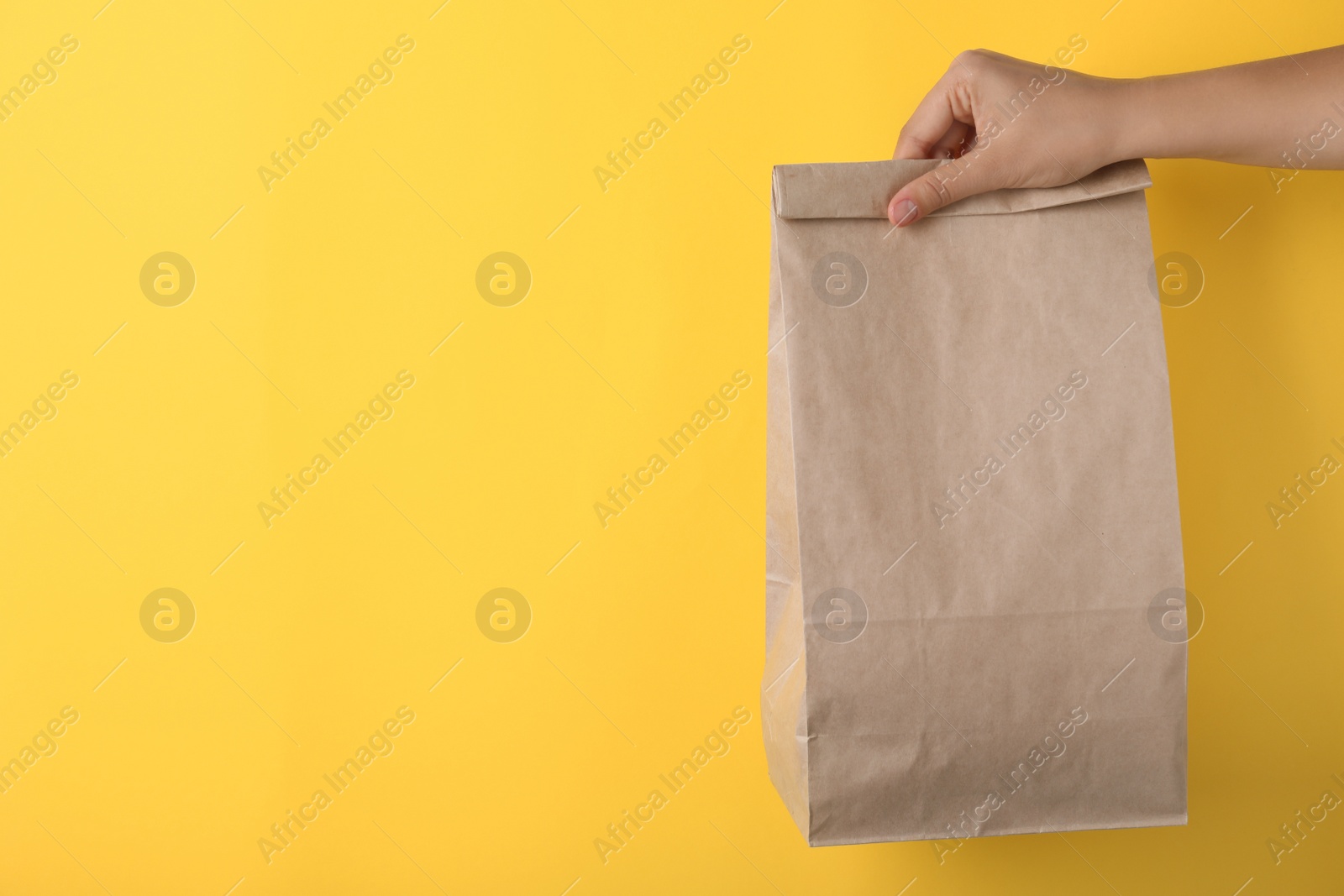 Photo of Woman holding paper bag on yellow background, closeup. Space for text