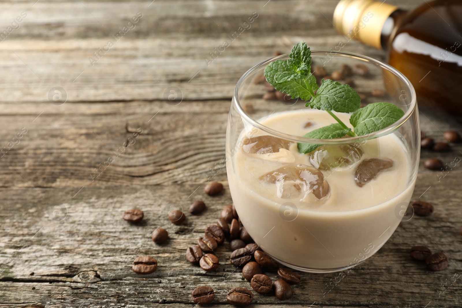 Photo of Coffee cream liqueur in glass, beans and mint on wooden table, closeup. Space for text