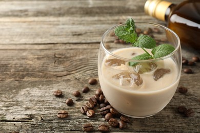 Coffee cream liqueur in glass, beans and mint on wooden table, closeup. Space for text