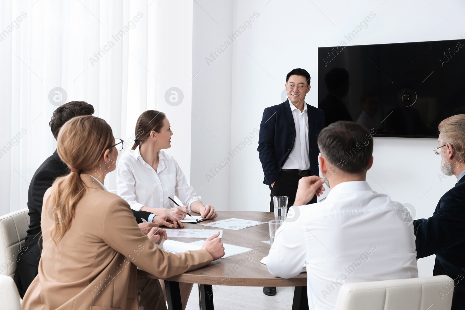 Photo of Business conference. Group of people listening to speaker report near tv screen in meeting room