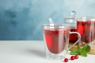 Photo of Tasty hot cranberry tea with mint and fresh berries on light table. Space for text