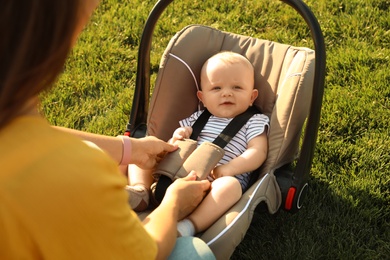 Photo of Mother fastening baby to child safety seat outdoors