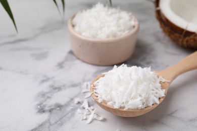 Photo of Coconut flakes in wooden spoon on white marble table, closeup. Space for text