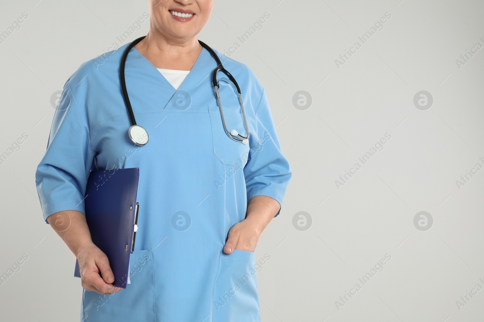 Photo of Mature doctor with clipboard on light grey background, closeup. Space for text