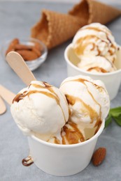 Scoops of ice cream with caramel sauce in paper cup on light grey table, closeup