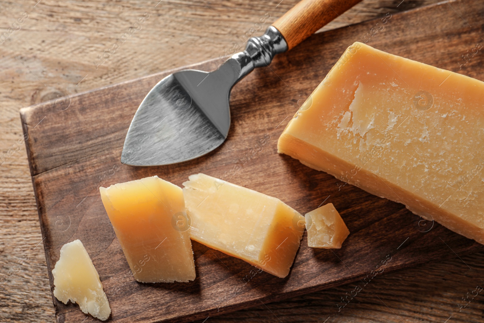 Photo of Board with cut Parmesan cheese on wooden table, top view