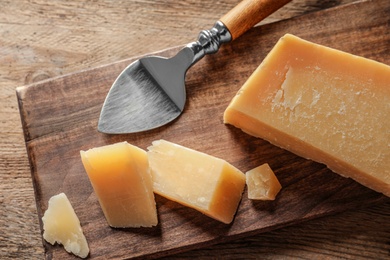 Board with cut Parmesan cheese on wooden table, top view