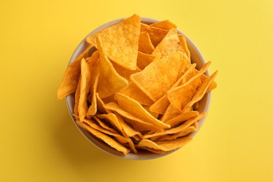 Photo of Tortilla chips (nachos) in bowl on yellow background, top view