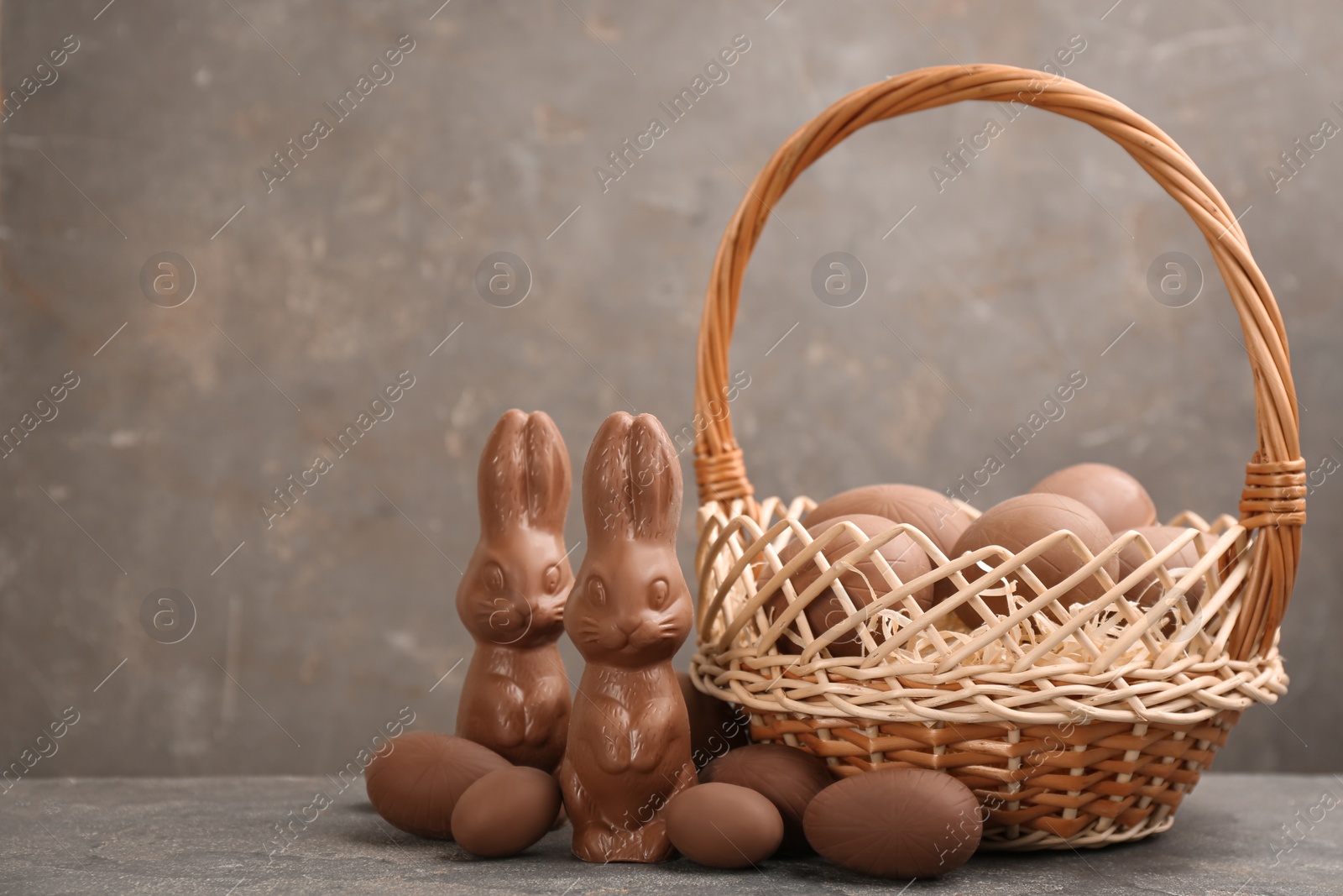 Photo of Chocolate Easter bunnies and eggs on grey table. Space for text