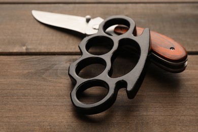 Photo of Black brass knuckles and knife on wooden background, closeup