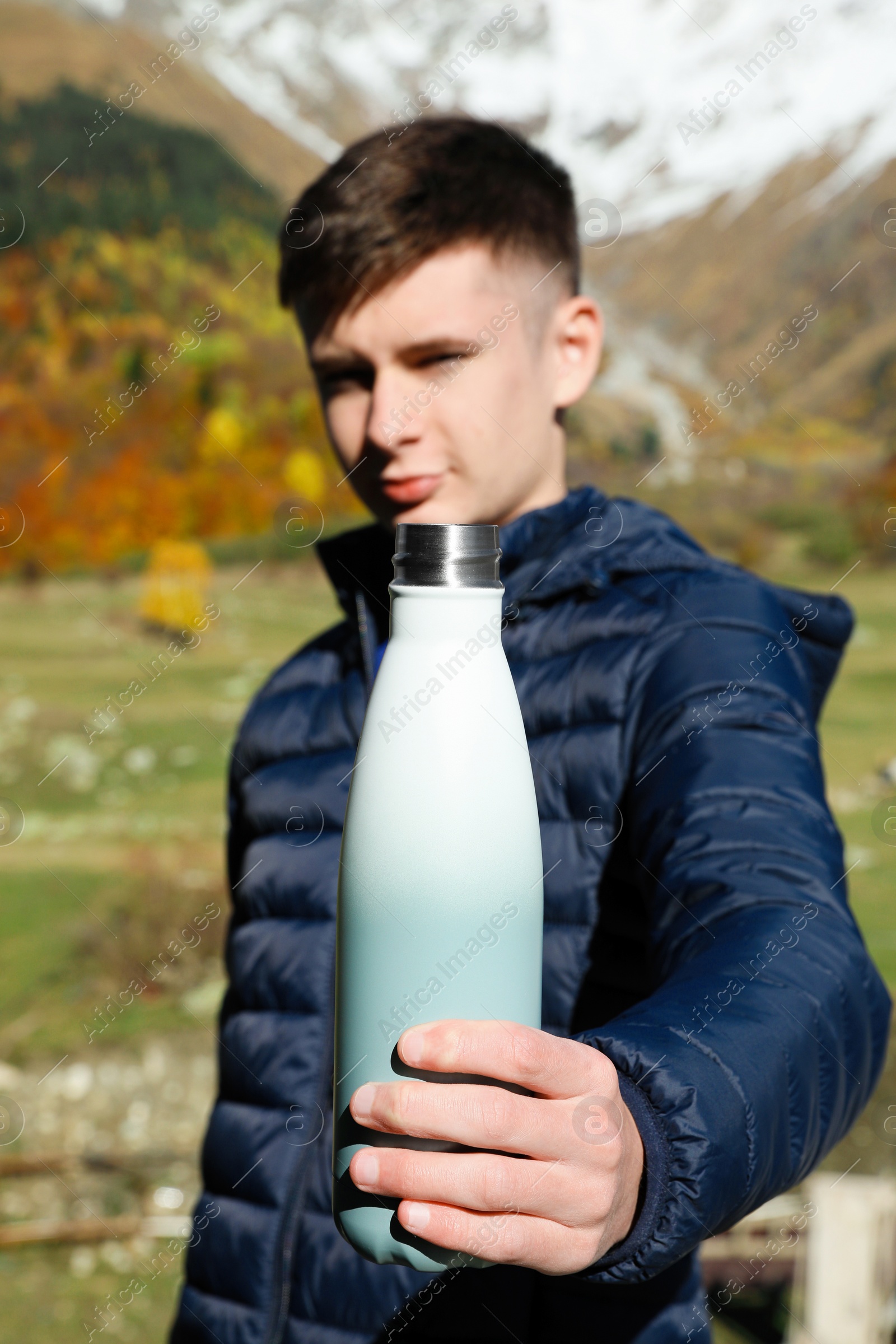 Photo of Boy holding thermo bottle with drink in mountains, focus on hand