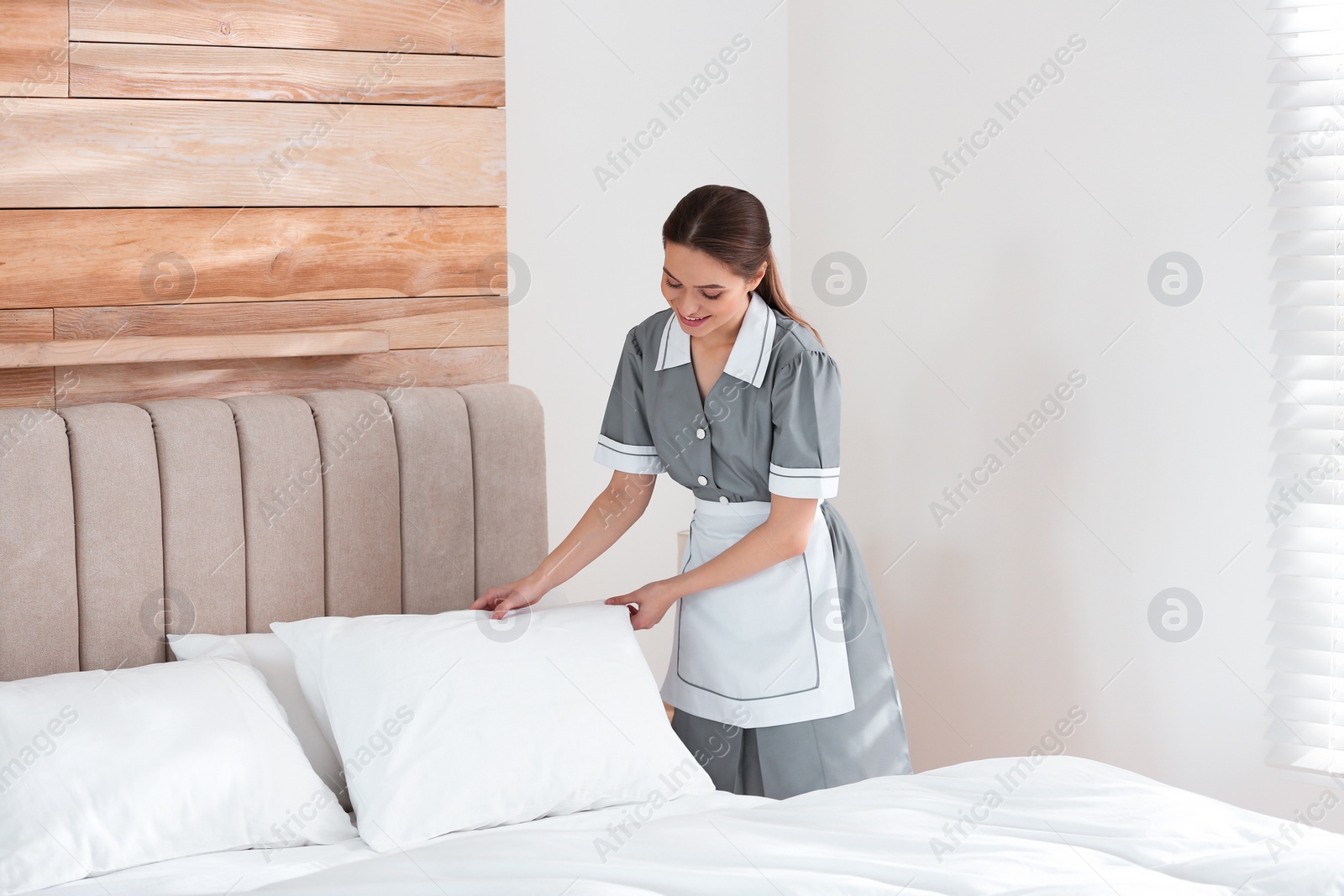 Photo of Young chambermaid making bed in hotel room