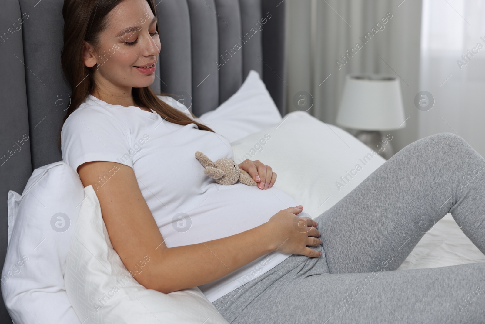 Photo of Beautiful pregnant woman with bunny toy on bed indoors