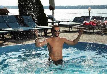 Photo of Handsome man having fun in outdoor swimming pool on summer day