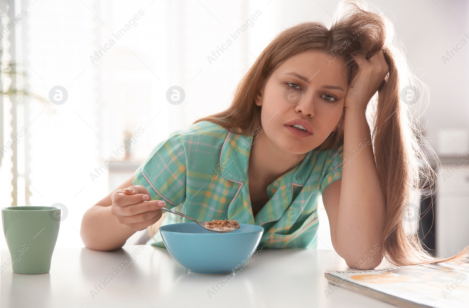 Photo of Sleepy young woman eating breakfast at home in morning