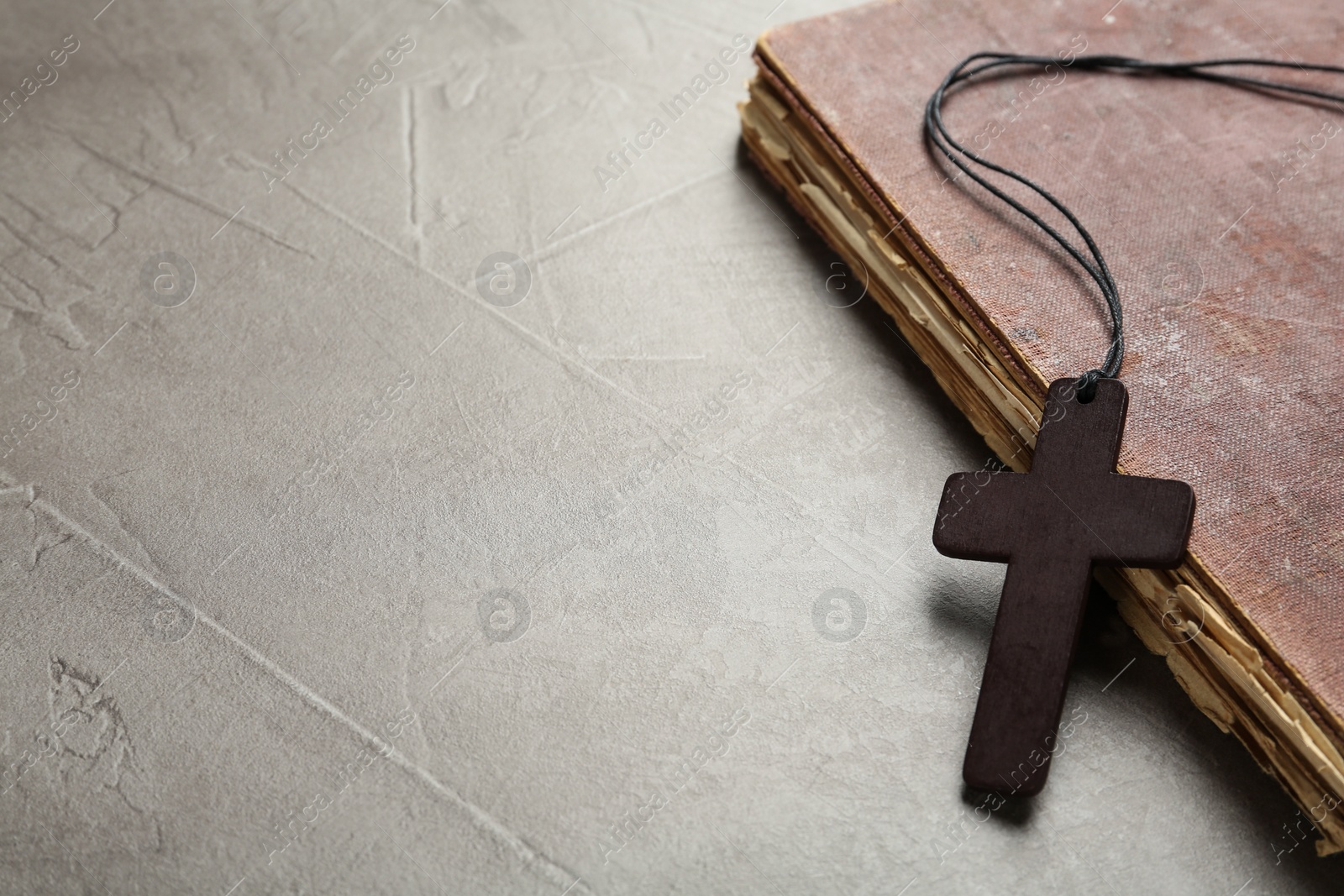 Photo of Wooden Christian cross and old Bible on grey table, space for text