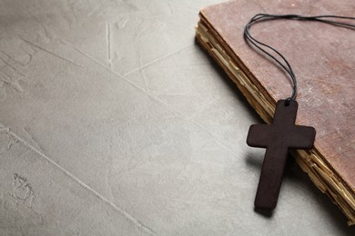 Photo of Wooden Christian cross and old Bible on grey table, space for text