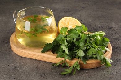 Photo of Aromatic tea, fresh parsley and lemon on grey table, closeup