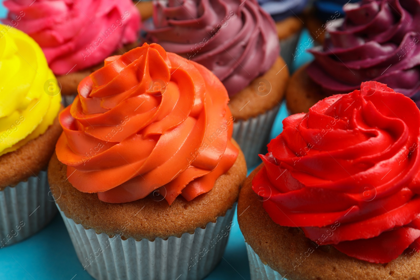 Photo of Many delicious colorful cupcakes on light blue background, closeup