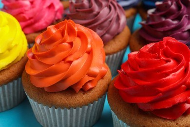 Many delicious colorful cupcakes on light blue background, closeup