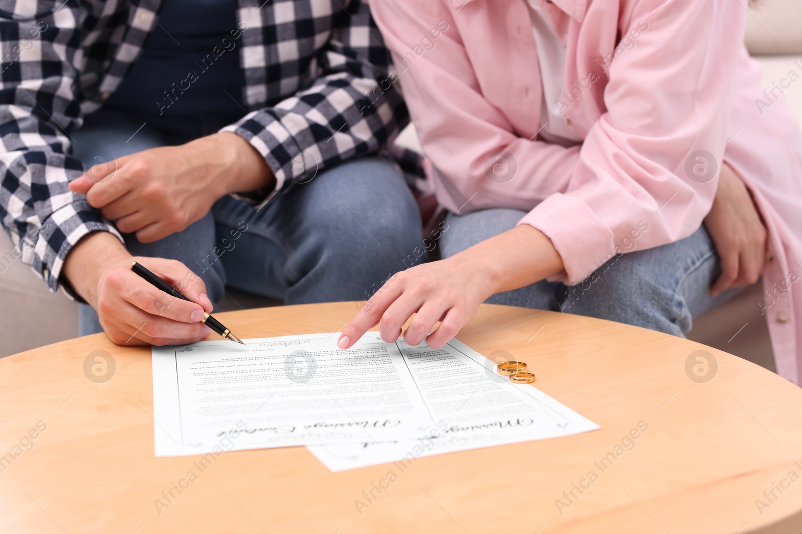 Photo of Man and woman signing marriage contract at wooden table indoors, closeup