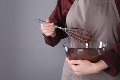 Photo of Woman with whisk making chocolate cream on grey background, closeup. Space for text